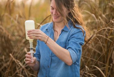 A woman pouring water from a larger sampling bottle into a smaller one.